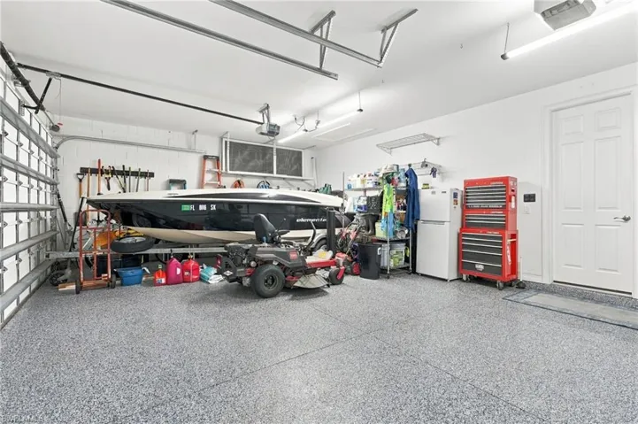Attached three-car garage featuring segmented overhead doors, durable epoxy-coated flooring, custom storage, and linear fluorescent lighting