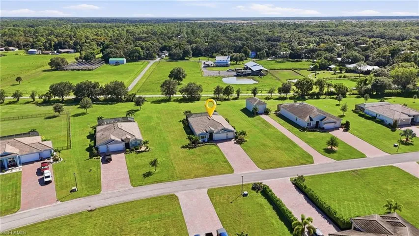 Aerial perspective featuring a single-story residence with a concrete tile roof, paver driveway, multi-car garage, and expansive lawn area