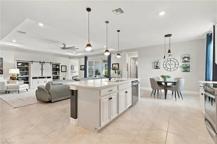 Kitchen featuring a central island with a stone-surface countertop, cabinetry with shaker-style detailing, recessed ceiling lighting, three pendant lights, and tile flooring