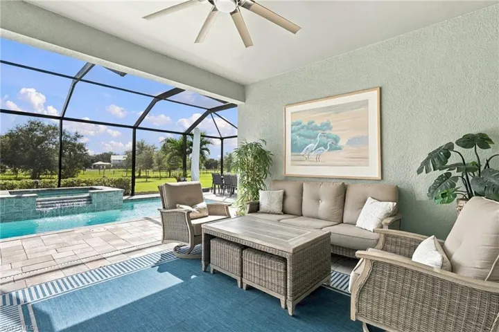 Covered lanai extends the living space outside featuring paver flooring, ceiling fan, built-in kitchenette with stone countertop and wine fridge, and glass sliding doors to the great room