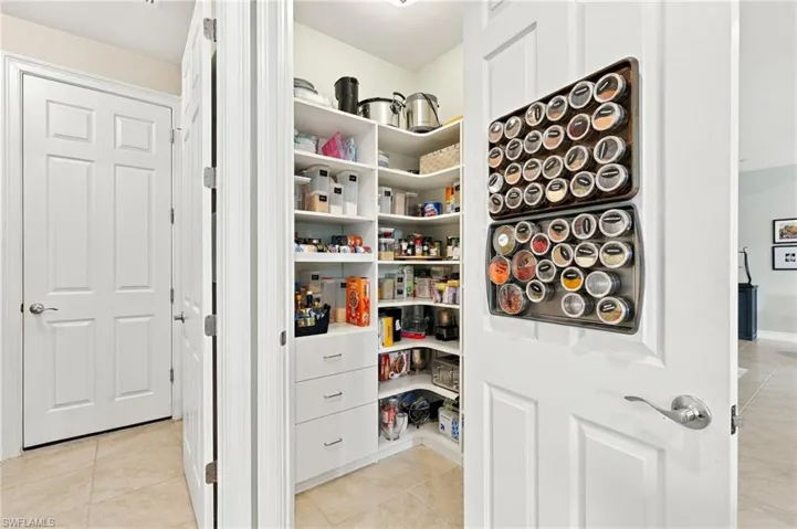 Walk-in pantry featuring white custom built-in shelving, multi-tiered corner storage, and three integrated lower storage drawers