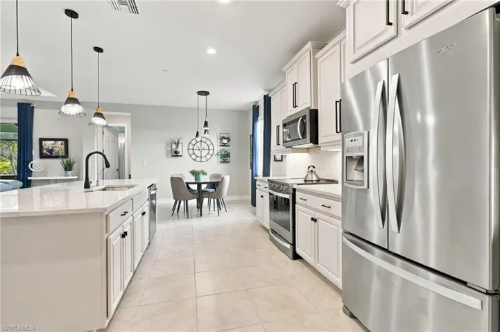 Kitchen featuring white cabinetry, stainless steel appliances, a kitchen island with stone-finish countertops, pendant lighting, and tile flooring