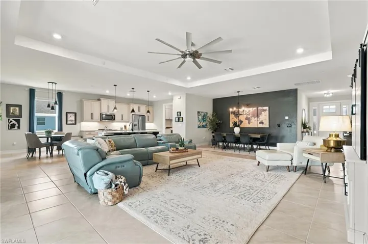 Open-concept interior featuring a tray ceiling, recessed lighting, tile flooring, and custom cabinetry with stainless steel appliances