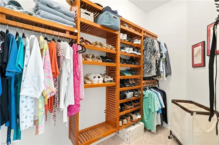 Primary bedroom walk-in closet featuring custom, multi-tiered natural wood shelving, dedicated hanging rods, and integrated shoe storage