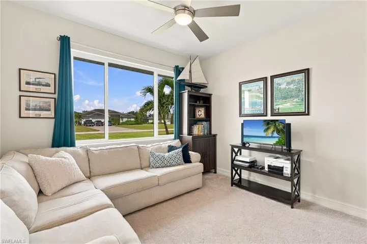 Bright and inviting fourth bedroom is being used as a den and features large multi-pane window at the front of the house and a ceiling-mounted light fixture with fan