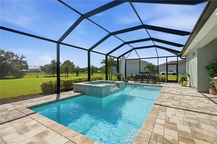 Screened-in pool area featuring a salt water pool with elevated spillover spa, stone-finish paver decking, and a spacious covered lanai