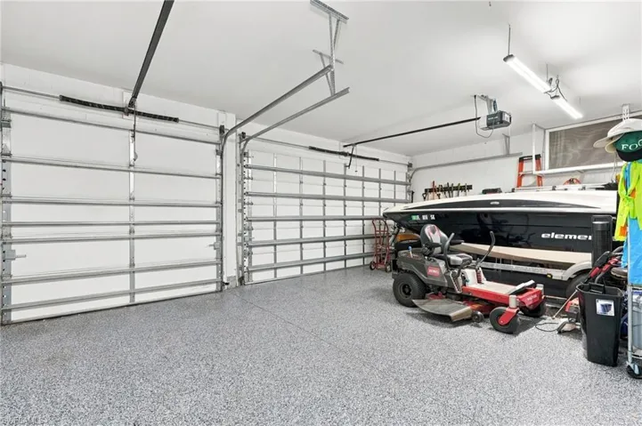 Attached three-car garage featuring segmented overhead doors, durable epoxy-coated flooring, custom storage, and linear fluorescent lighting