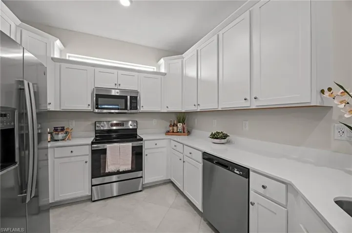 Kitchen featuring stainless steel appliances, light countertops, white cabinetry, and light tile patterned flooring