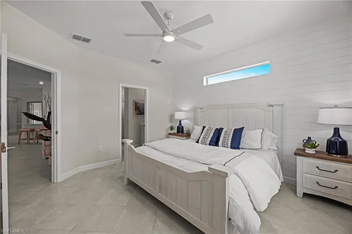 Bedroom with light tile patterned floors, a skylight, a ceiling fan, connected bathroom, and wood walls