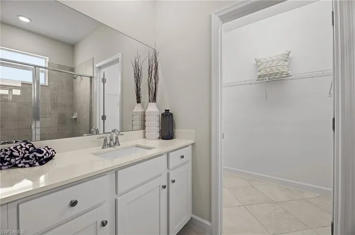 Bathroom with a walk in closet, vanity, a stall shower, and tile patterned flooring