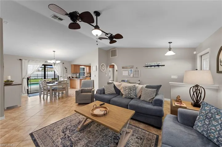 Living room featuring a ceiling fan, arched walkways, lofted ceiling, a chandelier, and light tile patterned flooring