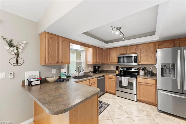 Kitchen with appliances with stainless steel finishes, a peninsula, a raised ceiling, and light tile patterned floors