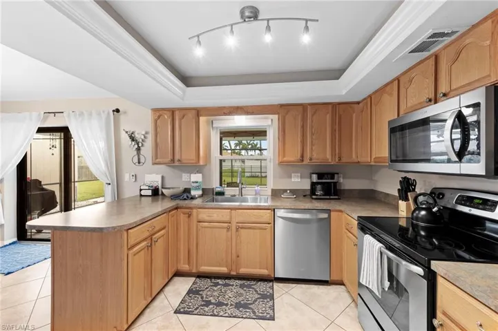 Kitchen with stainless steel appliances, a peninsula, a tray ceiling, track lighting, and light tile patterned floors