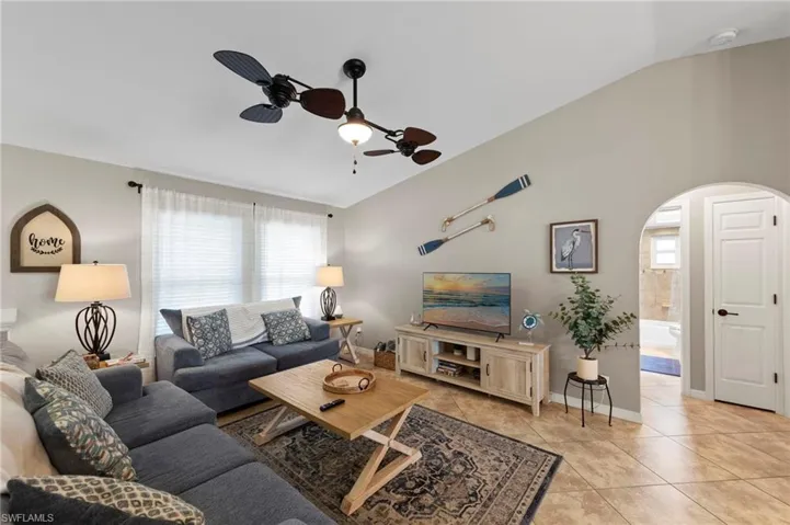 Living area featuring vaulted ceiling, arched walkways, a ceiling fan, and light tile patterned floors