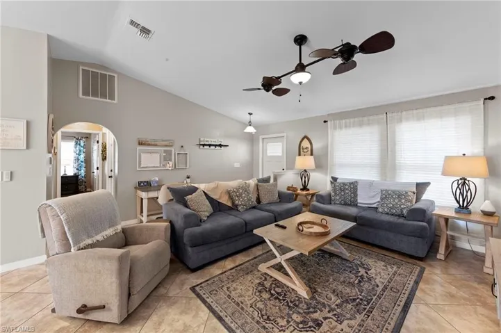 Living area with arched walkways, vaulted ceiling, a ceiling fan, and light tile patterned flooring