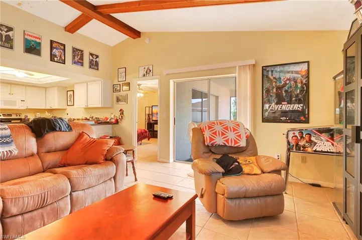 Tiled living room featuring ceiling fan and lofted ceiling with beams