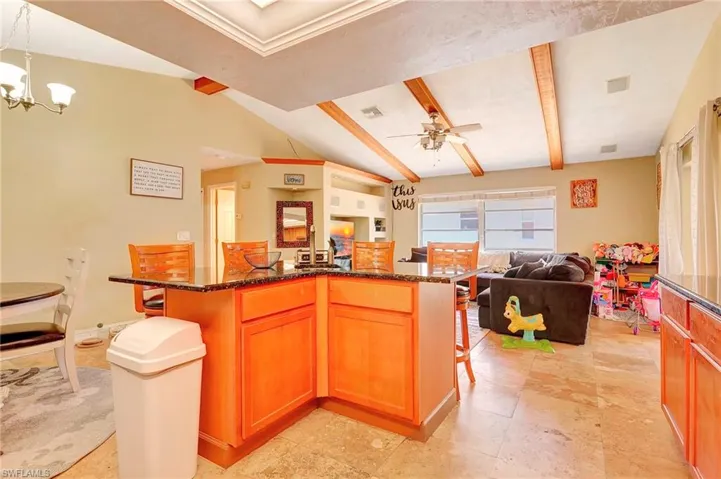 Kitchen with vaulted ceiling with beams, pendant lighting, dark stone countertops, ceiling fan with notable chandelier, and light tile floors