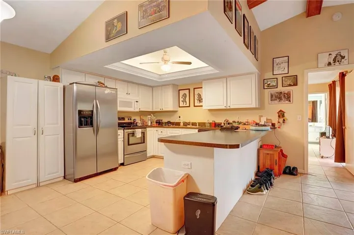 Kitchen with lofted ceiling, stainless steel appliances, kitchen peninsula, ceiling fan, and light tile floors