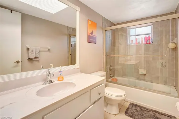 Full bathroom featuring vanity with extensive cabinet space, combined bath / shower with glass door, toilet, and tile floors