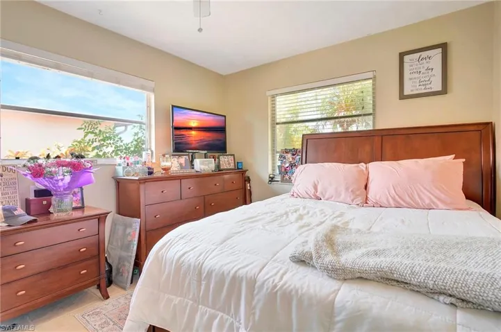 Bedroom featuring ceiling fan, multiple windows, and light tile floors