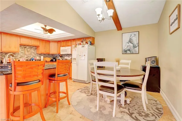 Tiled dining room featuring lofted ceiling, a raised ceiling, and ceiling fan with notable chandelier