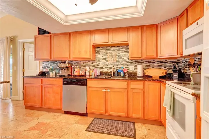 Kitchen featuring a raised ceiling, tasteful backsplash, white appliances, and light tile floors