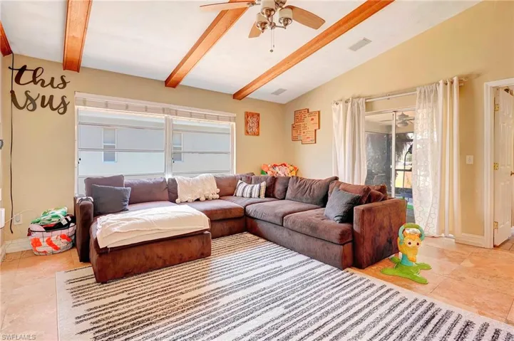 Living room with tile flooring, lofted ceiling with beams, and ceiling fan