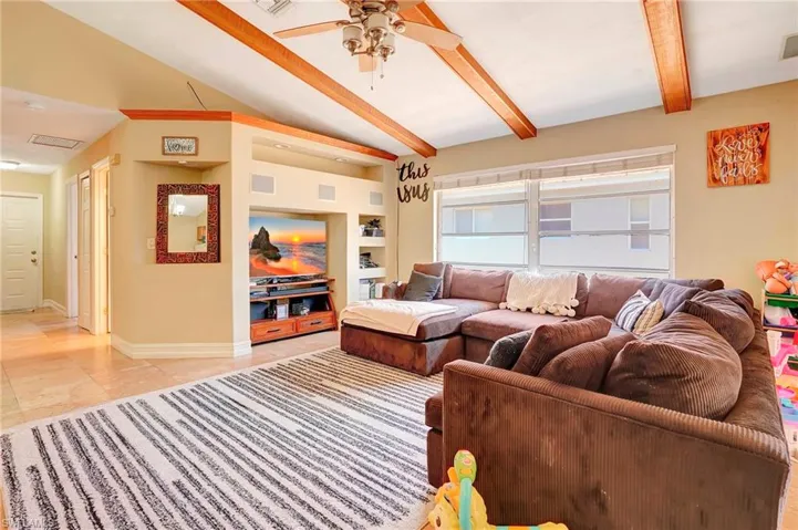 Living room featuring tile flooring, built in features, ceiling fan, and beam ceiling