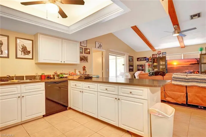 Kitchen featuring ceiling fan, vaulted ceiling with beams, black dishwasher, light tile floors, and white cabinetry