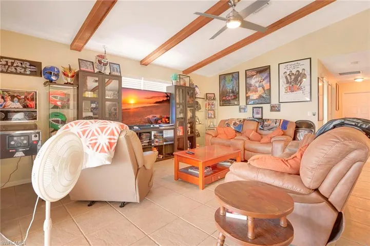 Tiled living room with lofted ceiling with beams and ceiling fan