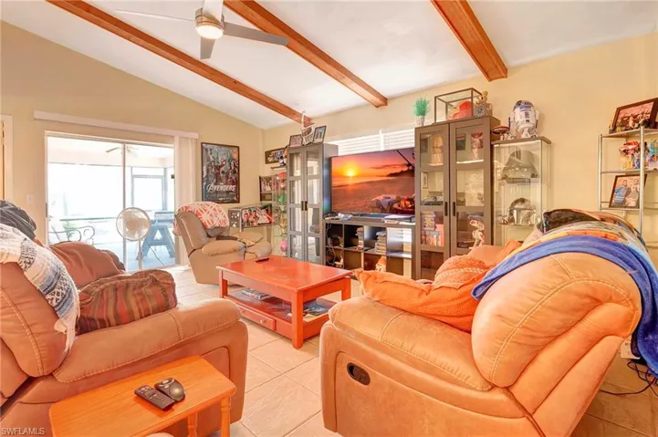Living room featuring vaulted ceiling with beams, ceiling fan, and light tile floors