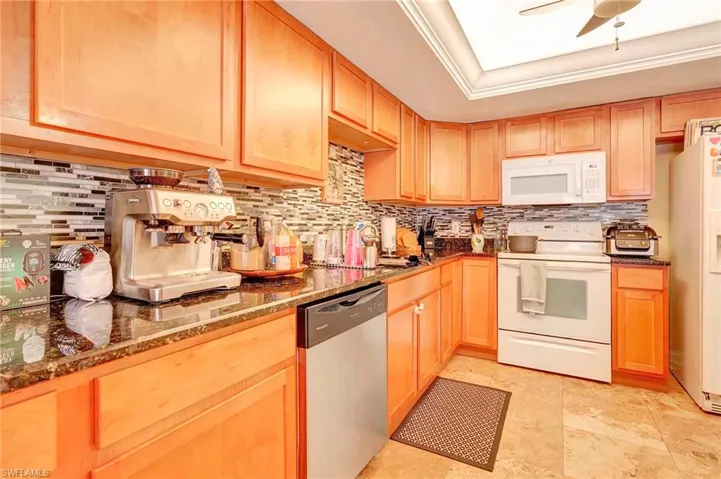 Kitchen with dark stone countertops, white appliances, backsplash, ceiling fan, and light tile floors