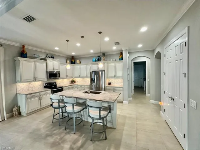 Kitchen with an island with sink, light stone countertops, stainless steel appliances, decorative light fixtures, and sink