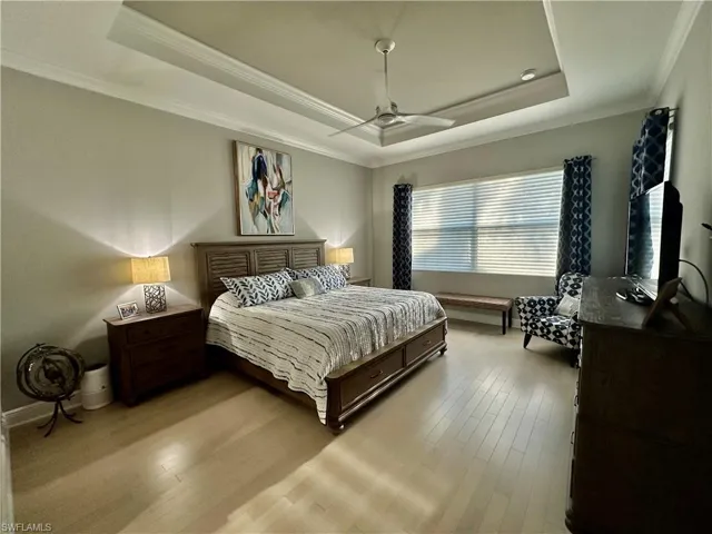 Bedroom featuring ornamental molding, light wood-type flooring, a tray ceiling, and ceiling fan