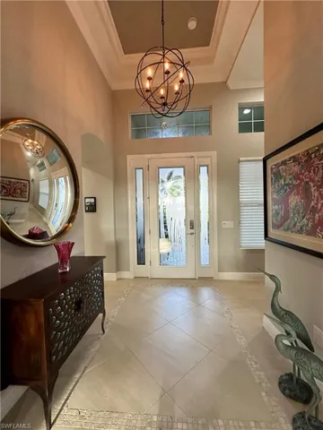 Tiled entryway featuring an inviting chandelier, a towering ceiling, a raised ceiling, and crown molding