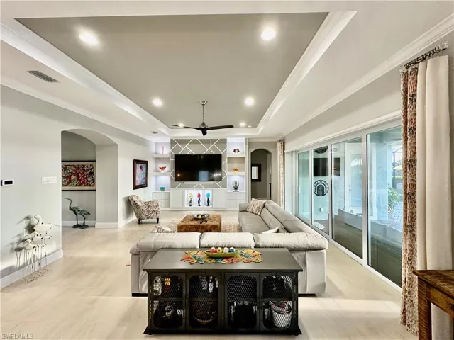 Living room with ceiling fan, a tray ceiling, and ornamental molding