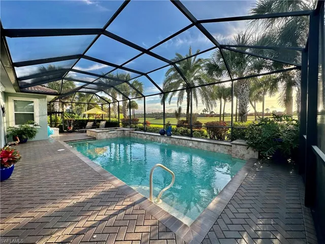 Pool at dusk with glass enclosure and a patio area