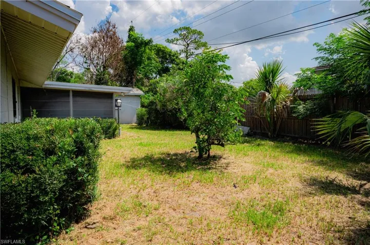 Expansive rear yard featuring green lawn, established perimeter shrubbery, mature trees, a privacy fence, and a screened patio