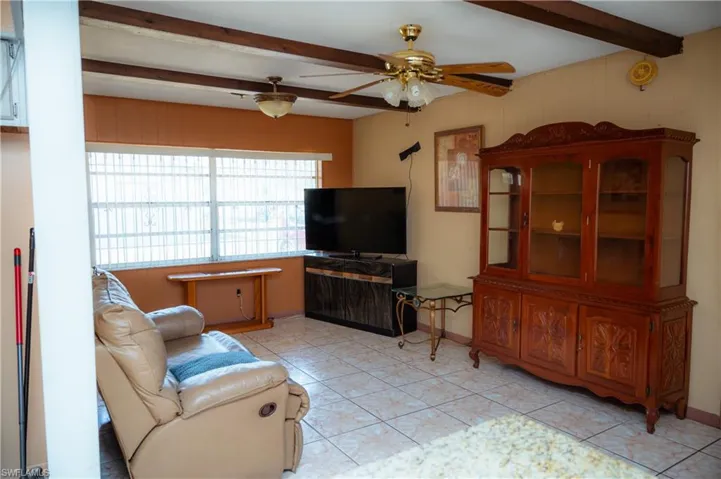 Open living area featuring exposed ceiling beams, a ceiling fan with light fixture, and tile flooring