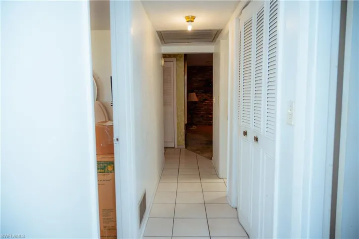 Hallway featuring white square tile flooring, white louvered bifold closet doors, and recessed ceiling light fixture