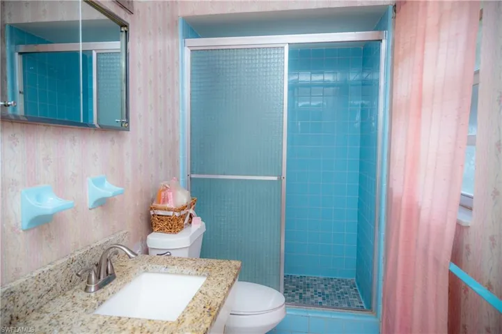 Bathroom featuring a blue tiled shower with a sliding glass door, a vanity with a stone-finish countertop, an undermount sink, and a mirrored medicine cabinet