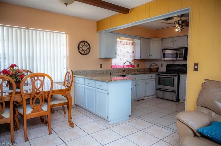 Open-concept kitchen featuring light-toned cabinetry, granite countertops, tile flooring, and stainless steel appliances
