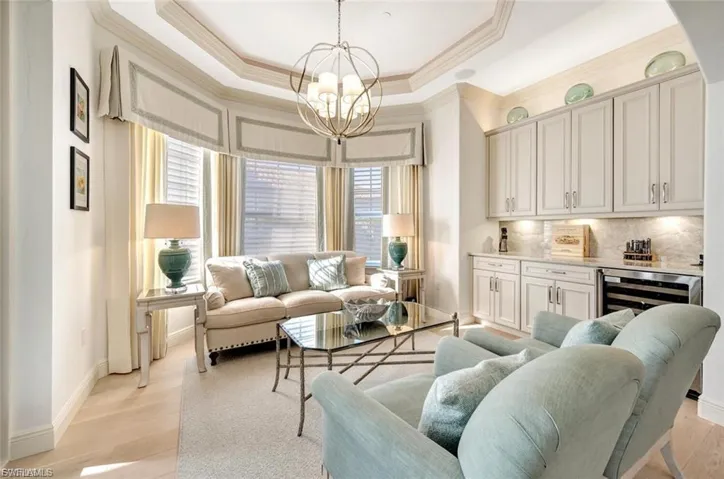Living area featuring hanging lights, crown molding, wine cooler, light wood-style floors, and a raised ceiling