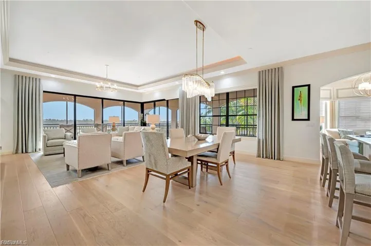 Dining space featuring suspended lighting, crown molding, light wood-type flooring, arched walkways, and a tray ceiling