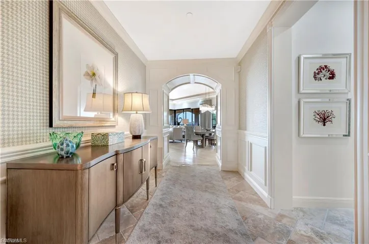 Hall featuring a decorative wall, arched walkways, wallpapered walls, a wainscoted wall, and crown molding