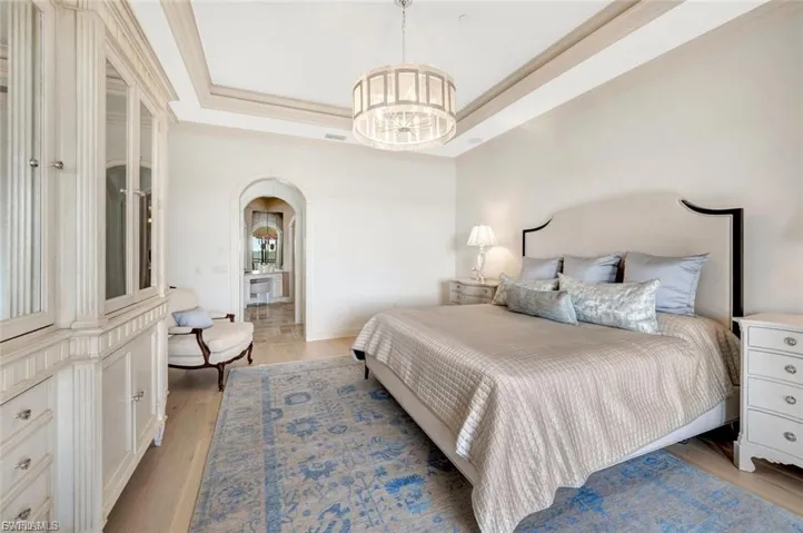 Bedroom with arched walkways, a tray ceiling, light wood-type flooring, hanging lights, and ornamental molding
