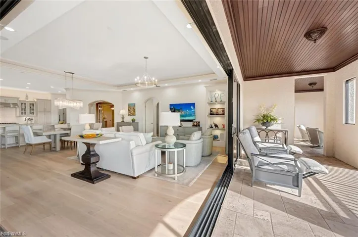 Living room featuring arched walkways, suspended lighting, crown molding, and stone tile floors