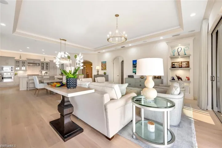 Living area with arched walkways, hanging lights, light wood-type flooring, a tray ceiling, and crown molding