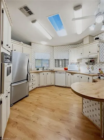 Kitchen with a textured ceiling, light countertops, white appliances, light wood-style flooring, and wallpapered walls