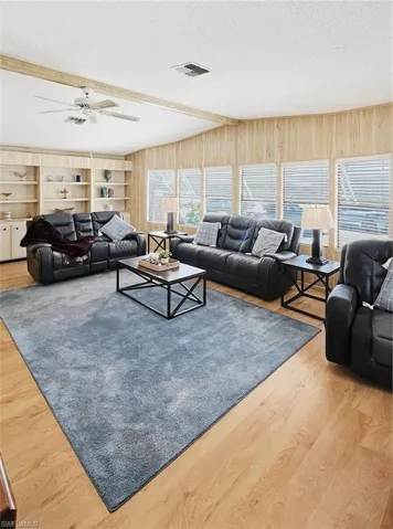 Living area with a textured ceiling, light wood-style floors, a ceiling fan, and beamed ceiling